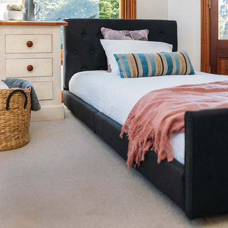 A low electric bed with a black headboard and footboard, featuring an expandable sleeping surface, partial wheel locking system, and is accompanied by pillows and a blanket.